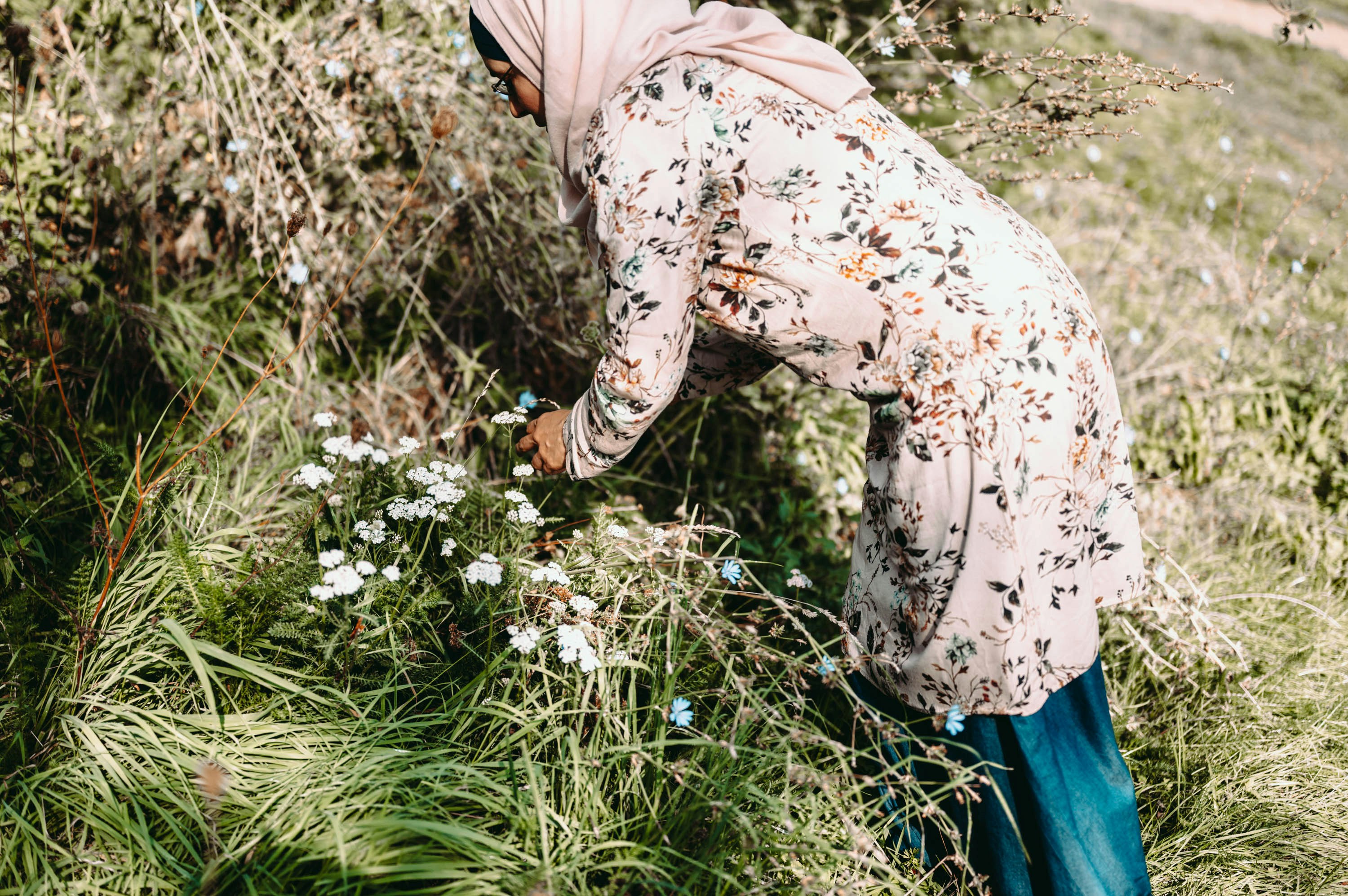 woman in beige and brown floral long sleeve shirt and blue denim jeans standing on green